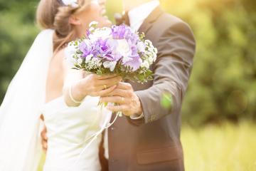 A bride and groom holding a bouquet of purple and white flowers, standing outdoors in a sunny garden setting, symbolizing love and joy on their wedding day : Stock Photo or Stock Video Download rcfotostock photos, images and assets rcfotostock | RC Photo Stock.: