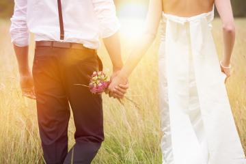 A bride and groom holding hands in a sunny meadow, with the groom carrying a small bouquet of wildflowers, symbolizing love, romance, and the beginning of a new journey together : Stock Photo or Stock Video Download rcfotostock photos, images and assets rcfotostock | RC Photo Stock.: