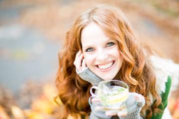 A cheerful red-haired woman holding a glass cup of herbal tea with lemon, wearing cozy fall clothing, smiling warmly, and surrounded by blurred autumn leaves in a soft natural background : Stock Photo or Stock Video Download rcfotostock photos, images and assets rcfotostock | RC Photo Stock.: