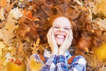 A cheerful red-haired woman lying in a pile of autumn leaves, smiling brightly, with her hair spread out and hands on her cheeks, surrounded by warm fall colors : Stock Photo or Stock Video Download rcfotostock photos, images and assets rcfotostock | RC Photo Stock.: