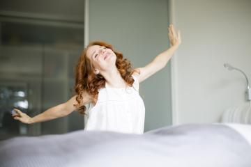 A cheerful woman with red curly hair stretching happily in the morning, standing in a bright bedroom, radiating positive energy and embracing the start of a new day : Stock Photo or Stock Video Download rcfotostock photos, images and assets rcfotostock | RC Photo Stock.: