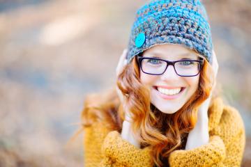 A cheerful woman with red hair wearing glasses, a crocheted blue and brown hat with a button, and a mustard sweater, smiling warmly in an autumn outdoor setting : Stock Photo or Stock Video Download rcfotostock photos, images and assets rcfotostock | RC Photo Stock.: