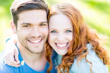 A cheerful young couple smiling brightly in a sunny outdoor setting, showcasing their happiness and love, with green grass and natural light enhancing the joyful moment- Stock Photo or Stock Video of rcfotostock | RC Photo Stock