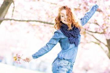 A cheerful young woman with red curly hair enjoying spring, wearing a denim outfit and polka dot scarf, holding cherry blossoms, surrounded by blooming trees and sunlight : Stock Photo or Stock Video Download rcfotostock photos, images and assets rcfotostock | RC Photo Stock.:
