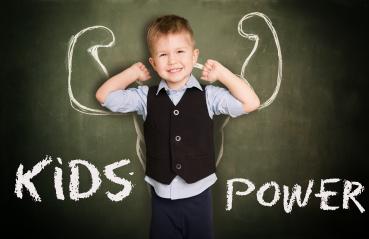 A confident boy smiling in front of a chalkboard with drawn muscular arms, symbolizing strength and empowerment, with the words 