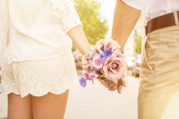 A couple holding hands in a romantic setting, with one person holding a bouquet of pink roses and purple flowers, symbolizing love and affection, in soft, warm lighting outdoors- Stock Photo or Stock Video of rcfotostock | RC Photo Stock