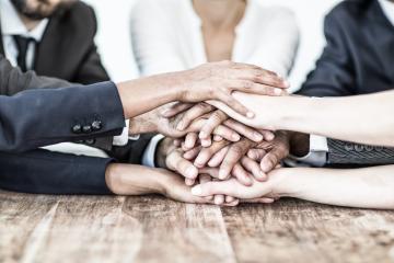 A diverse group of hands stacked together over a wooden table, symbolizing teamwork, unity, collaboration, and solidarity in a professional or community setting : Stock Photo or Stock Video Download rcfotostock photos, images and assets rcfotostock | RC Photo Stock.: