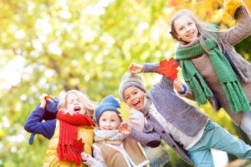 A group of cheerful children enjoying an autumn day, wearing cozy scarves and hats, holding colorful fall leaves, and playing together in a vibrant outdoor setting surrounded by trees- Stock Photo or Stock Video of rcfotostock | RC Photo Stock