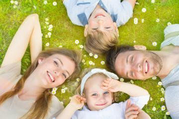 A happy family of four lies on the grass surrounded by daisies, smiling and enjoying quality time outdoors, creating a moment of togetherness, relaxation, and nature bonding : Stock Photo or Stock Video Download rcfotostock photos, images and assets rcfotostock | RC Photo Stock.: