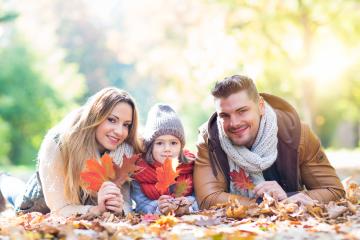 A happy family of three lying on colorful autumn leaves in a sunny park, holding vibrant red and orange leaves, dressed warmly with scarves and hats, enjoying quality time together in nature- Stock Photo or Stock Video of rcfotostock | RC Photo Stock