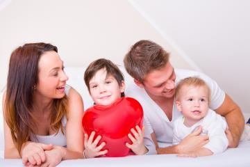 A happy family spending quality time together on a bed, with a young boy holding a large red heart, symbolizing love, bonding, and warmth in a cozy indoor setting
 : Stock Photo or Stock Video Download rcfotostock photos, images and assets rcfotostock | RC Photo Stock.: