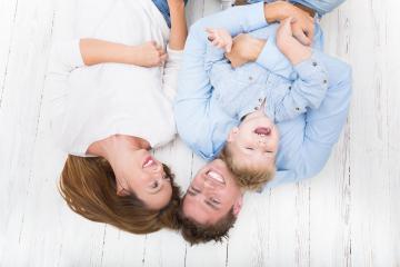 A joyful family of three lies on a white wooden floor, smiling and laughing together, with the child playfully interacting between the parents in a heartwarming and fun moment. : Stock Photo or Stock Video Download rcfotostock photos, images and assets rcfotostock | RC Photo Stock.: