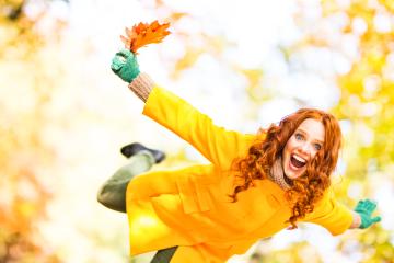A joyful red-haired woman in a yellow coat, playfully holding autumn leaves, smiling brightly, and enjoying the fall season with vibrant colors in an outdoor setting- Stock Photo or Stock Video of rcfotostock | RC Photo Stock