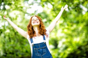A joyful red-haired woman in denim overalls with arms raised, smiling brightly in a lush green outdoor setting, celebrating happiness and freedom in nature : Stock Photo or Stock Video Download rcfotostock photos, images and assets rcfotostock | RC Photo Stock.: