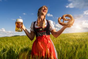 A joyful woman in a traditional Bavarian dress holding a beer and a pretzel in a wheat field celebrating Oktoberfest or dult festival in munich.- Stock Photo or Stock Video of rcfotostock | RC Photo Stock