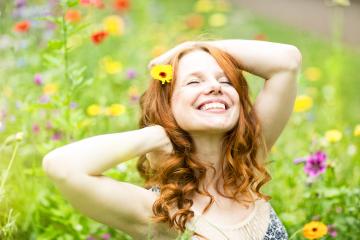 A joyful woman with red curly hair and a yellow flower in her hair, smiling and enjoying a sunny day in a vibrant meadow filled with colorful wildflowers, radiating happiness and serenity- Stock Photo or Stock Video of rcfotostock | RC Photo Stock
