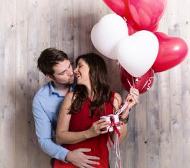 A loving couple celebrating with heart-shaped balloons, sharing a joyful kiss while holding a gift, surrounded by a warm wooden background, exuding love and happiness- Stock Photo or Stock Video of rcfotostock | RC Photo Stock