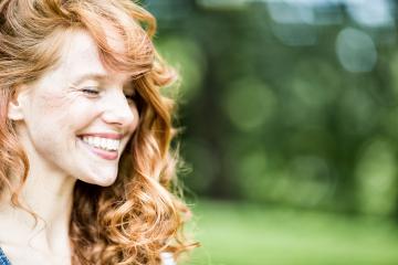 A red-haired woman with curly hair, smiling brightly in a natural outdoor setting, radiating happiness and beauty, with a blurred green background enhancing the serene mood : Stock Photo or Stock Video Download rcfotostock photos, images and assets rcfotostock | RC Photo Stock.: