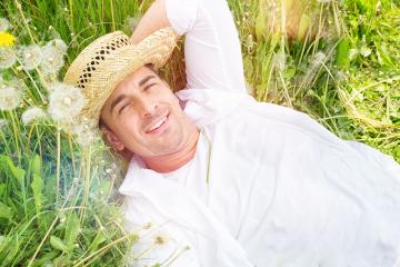 A relaxed man in a straw hat and white shirt lying on a grassy field surrounded by dandelions, enjoying a sunny day in nature, radiating calmness and happiness- Stock Photo or Stock Video of rcfotostock | RC Photo Stock