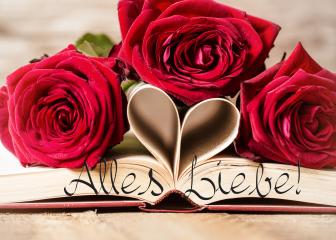 A romantic arrangement featuring three red roses, a book with folded pages forming a heart, and the text 