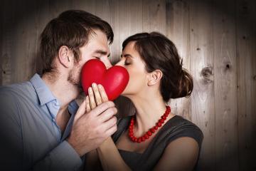 A romantic couple sharing a kiss while holding a red heart together in front of them, set against a rustic wooden background, symbolizing love, intimacy, and a special connection : Stock Photo or Stock Video Download rcfotostock photos, images and assets rcfotostock | RC Photo Stock.: