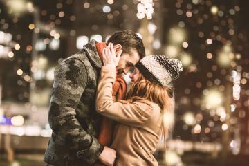 A romantic couple sharing an intimate moment outdoors on a winter night with warm clothing, festive lights, and a cozy atmosphere filled with bokeh- Stock Photo or Stock Video of rcfotostock | RC Photo Stock