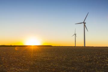 A scenic view of two wind turbines standing tall in an open field during sunset, with golden sunlight casting a warm glow over the landscape and a clear sky transitioning into dusk : Stock Photo or Stock Video Download rcfotostock photos, images and assets rcfotostock | RC Photo Stock.: