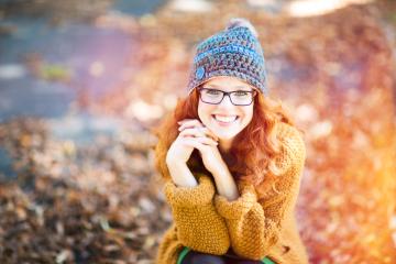 A smiling red-haired woman wearing glasses and a crocheted hat, sitting outdoors in autumn surrounded by warm tones and fallen leaves, exuding warmth and joy : Stock Photo or Stock Video Download rcfotostock photos, images and assets rcfotostock | RC Photo Stock.: