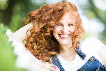 A smiling red-haired woman with curly hair enjoying a sunny outdoor moment, wearing denim overalls and lying on the grass, exuding joy and natural beauty with a vibrant background : Stock Photo or Stock Video Download rcfotostock photos, images and assets rcfotostock | RC Photo Stock.: