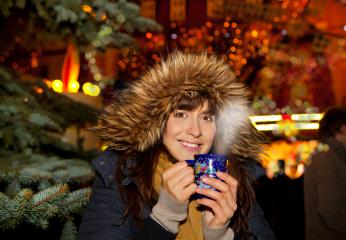 A smiling woman in a cozy fur-lined hood enjoying a hot drink at a festive Christmas market, surrounded by twinkling lights and a holiday ambiance with a decorated tree in the background : Stock Photo or Stock Video Download rcfotostock photos, images and assets rcfotostock | RC Photo Stock.: