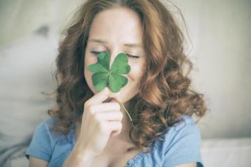 A smiling woman with red curly hair playfully holding a four-leaf clover over her nose, symbolizing happiness, luck, and positivity in a soft and light indoor setting : Stock Photo or Stock Video Download rcfotostock photos, images and assets rcfotostock | RC Photo Stock.: