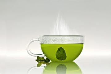 A steaming glass cup of green tea with a mint leaf inside and a few fresh mint leaves placed beside it on a reflective surface : Stock Photo or Stock Video Download rcfotostock photos, images and assets rcfotostock | RC Photo Stock.: