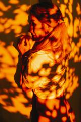 A woman with blonde hair is standing against a wall, bathed in warm, dappled orange light creating intricate shadow patterns on her face and body.
 : Stock Photo or Stock Video Download rcfotostock photos, images and assets rcfotostock | RC Photo Stock.:
