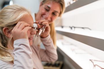 Adult assisting a child in trying on new eyeglasses at a optical store : Stock Photo or Stock Video Download rcfotostock photos, images and assets rcfotostock | RC Photo Stock.: