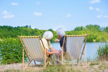 An elderly couple sitting on striped deck chairs by a serene lake, surrounded by lush greenery under a bright blue sky, enjoying a peaceful and relaxing moment in nature : Stock Photo or Stock Video Download rcfotostock photos, images and assets rcfotostock | RC Photo Stock.: