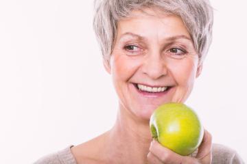 An older woman with short gray hair smiles while holding a green apple against a plain white background.- Stock Photo or Stock Video of rcfotostock | RC Photo Stock