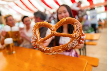 Asian woman holding a large pretzel at Oktoberfest, with mugs of beer in the background and colorful striped tent overhead in munich : Stock Photo or Stock Video Download rcfotostock photos, images and assets rcfotostock | RC Photo Stock.: