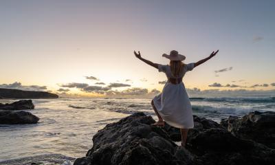 Back view of a woman in a white dress and straw hat with arms raised, standing on rocks at sunset by the ocean : Stock Photo or Stock Video Download rcfotostock photos, images and assets rcfotostock | RC Photo Stock.: