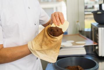 baker fills a piping bag with gingerbread dough using a scraper, preparing for the next step of piping the mixture onto wafers in a professional kitchen setting- Stock Photo or Stock Video of rcfotostock | RC Photo Stock