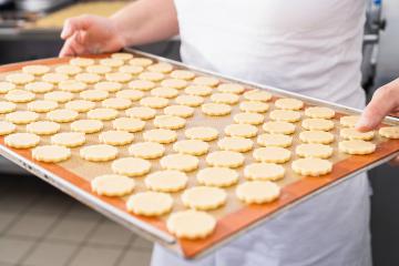 Baker holding a tray filled with unbaked, shaped cookie dough pieces on a silicone mat, preparing the cookies for baking in a professional bakery environment : Stock Photo or Stock Video Download rcfotostock photos, images and assets rcfotostock | RC Photo Stock.: