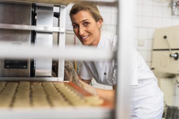 baker in a professional kitchen is smiling while placing a tray of cookies into an oven. The scene shows the baking process in action, emphasizing the joy of baking. : Stock Photo or Stock Video Download rcfotostock photos, images and assets rcfotostock | RC Photo Stock.: