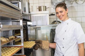 baker in a white uniform smiles while taking a tray of cookies from the oven. The kitchen setting is filled with baking equipment, creating a professional baking environment. : Stock Photo or Stock Video Download rcfotostock photos, images and assets rcfotostock | RC Photo Stock.: