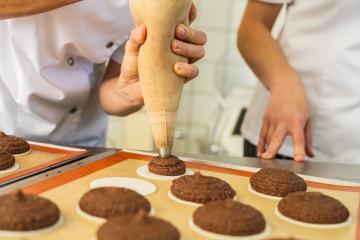 baker is piping gingerbread dough onto baking wafers using a piping bag, preparing the gingerbread rounds on a silicone mat for baking in a professional kitchen : Stock Photo or Stock Video Download rcfotostock photos, images and assets rcfotostock | RC Photo Stock.: