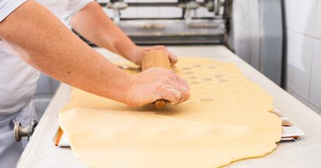 baker rolls out cookie dough on a work surface using a wooden rolling pin, preparing it for cutting shapes. The scene captures the hands-on baking process in a professional kitchen- Stock Photo or Stock Video of rcfotostock | RC Photo Stock