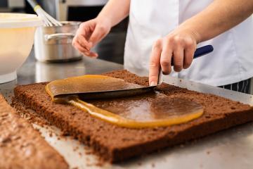 Baker spreading caramel on a chocolate sheet cake using a spatula in a bakery, preparing the dessert for layering in a professional baking environment- Stock Photo or Stock Video of rcfotostock | RC Photo Stock