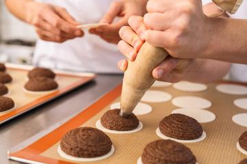 baker uses a piping bag to pipe gingerbread dough onto wafers on a baking sheet, while another baker prepares more wafers, in a professional kitchen setting : Stock Photo or Stock Video Download rcfotostock photos, images and assets rcfotostock | RC Photo Stock.: