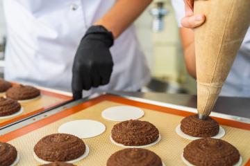 baker uses a piping bag to shape gingerbread dough onto round wafers, while another baker with a black glove assists in the process. The gingerbread cookies are being prepared for baking- Stock Photo or Stock Video of rcfotostock | RC Photo Stock