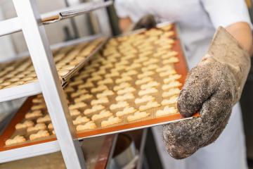 Baker wearing a glove and placing a tray of freshly baked cookies on a cooling rack in a bakery, using a silicone mat to support the cookies in a professional baking environment : Stock Photo or Stock Video Download rcfotostock photos, images and assets rcfotostock | RC Photo Stock.: