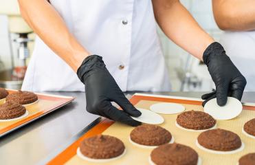 baker wearing black gloves is carefully placing wafers under freshly piped gingerbread dough on a baking sheet, preparing the cookies for baking in a commercial kitchen- Stock Photo or Stock Video of rcfotostock | RC Photo Stock