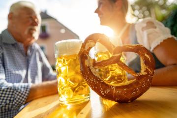 Bavarian Beer mugs and pretzel on table with senior man and woman in the background at beer garden, Munich, Germany- Stock Photo or Stock Video of rcfotostock | RC Photo Stock